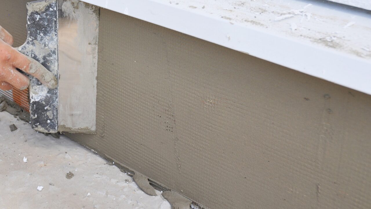 Contractor repairing a house foundation with plaster
